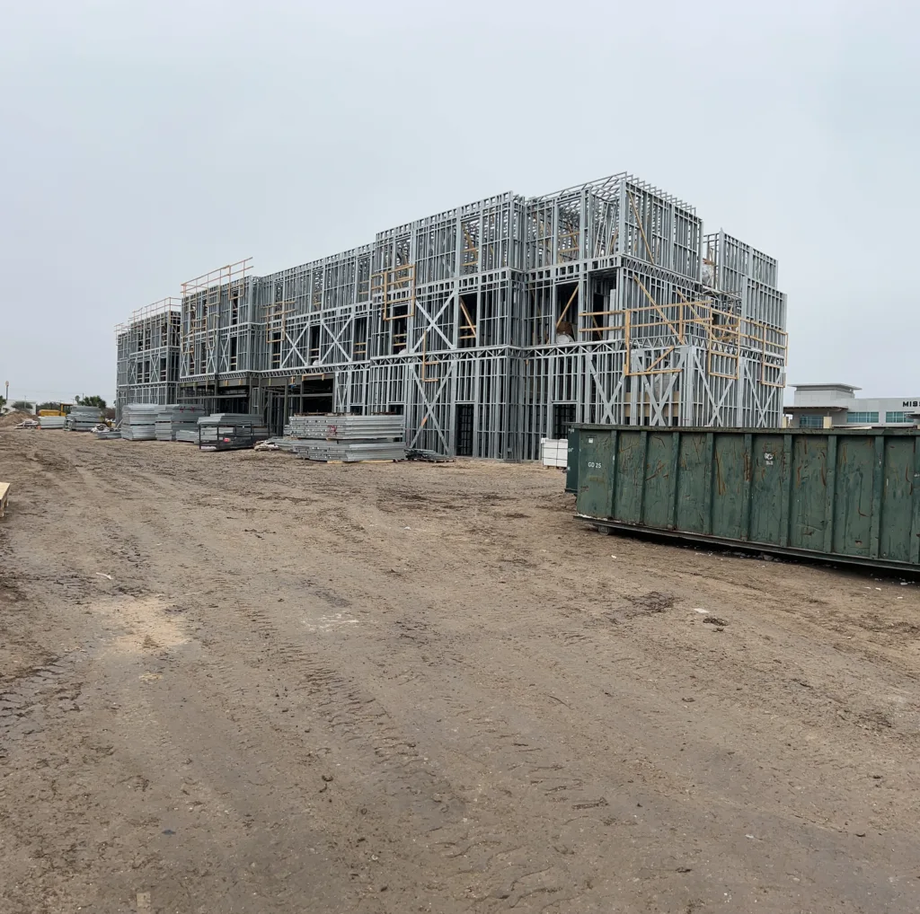 image00037 - Scottsdale Construction Systems Construction site with a multi-story steel frame building under construction on a dirt lot, with scattered materials nearby.