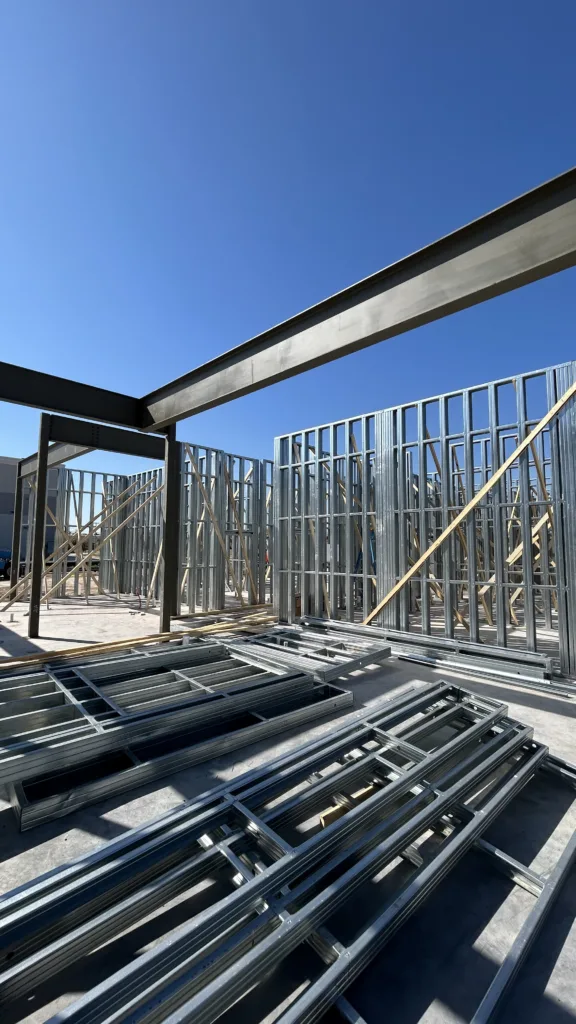 image00076 - Scottsdale Construction Systems Construction site with unfinished metal stud walls and steel beams against a blue sky, with wooden bracing and hardware on the floor