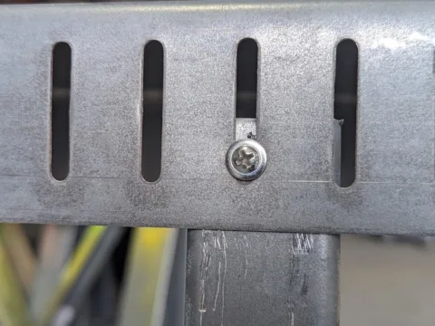 Low-profile pan-head screw riding in a vertical slot of galvanized slotted deflection track above a cold-formed steel stud, showing how slip track lets the floor above deflect, roll formed on a Scottsdale KFS Framemaker 1220G3 steel stud roll former, an Arkitech roll former alternative