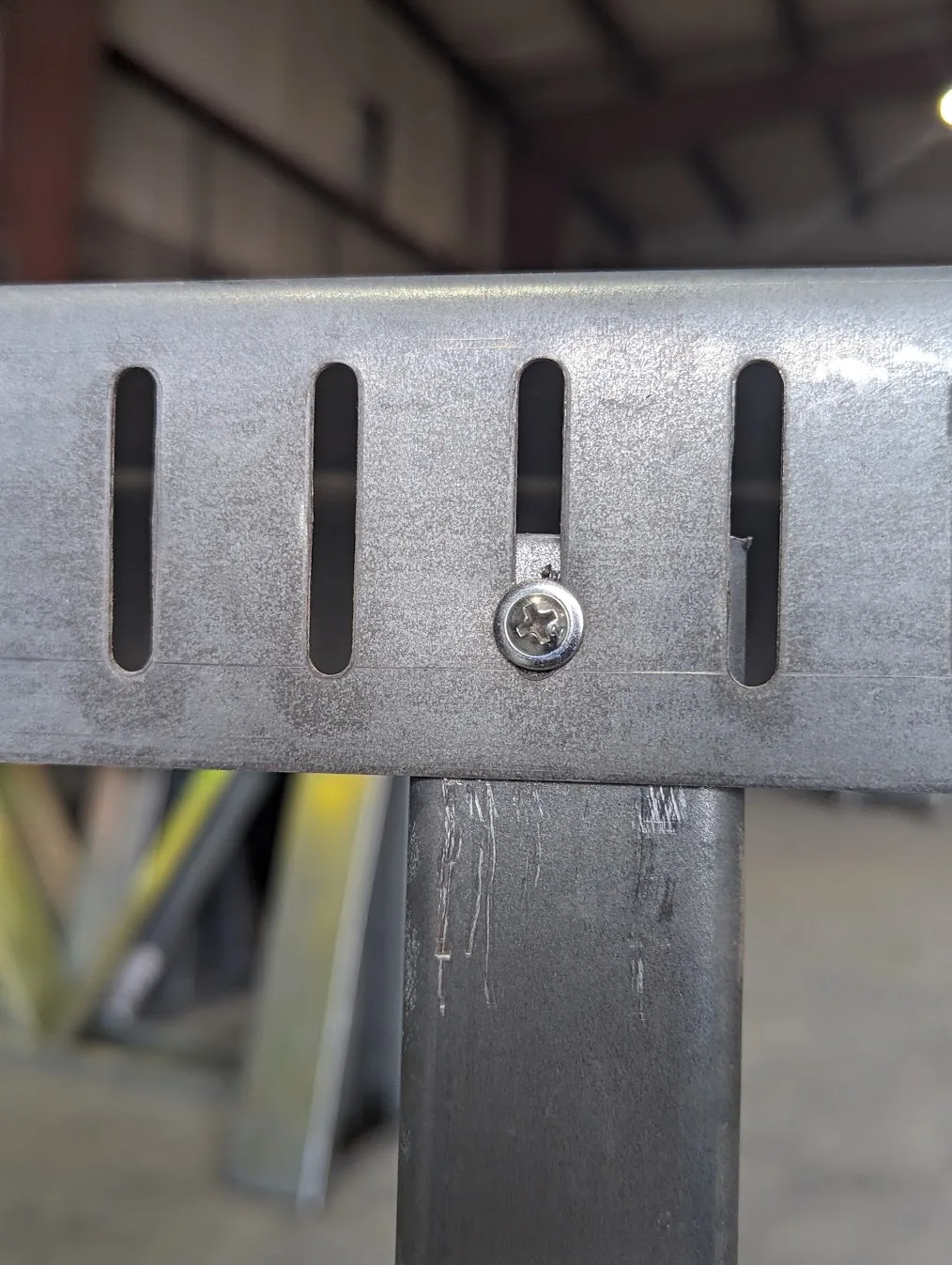 Low-profile pan-head screw riding in a vertical slot of galvanized slotted deflection track above a cold-formed steel stud, showing how slip track lets the floor above deflect, roll formed on a Scottsdale KFS Framemaker 1220G3 steel stud roll former, an Arkitech roll former alternative